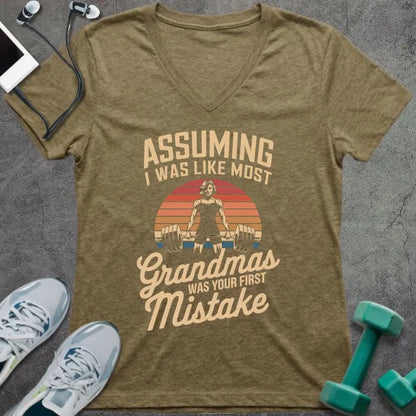 Heather olive t-shirt printed with "ASSUMING I WAS LIKE MOST Grandmas WAS YOUR FIRST Mistake" in cream, orange, red, black, with a muscular woman silhouette deadlifting over a retro sunset