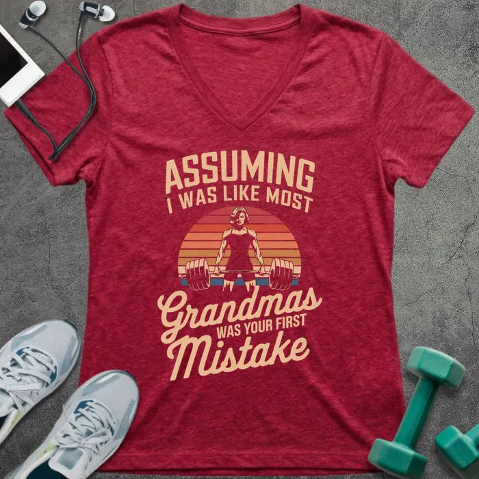 Heather red t-shirt printed with "ASSUMING I WAS LIKE MOST Grandmas WAS YOUR FIRST Mistake" in cream, orange, red, black, with a muscular woman silhouette deadlifting over a retro sunset