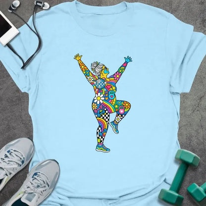 Light blue t-shirt printed with an older woman with a gray bun dancing with her arms up, her body filled with colorful flowers, rainbows, hearts, music notes and a disco ball