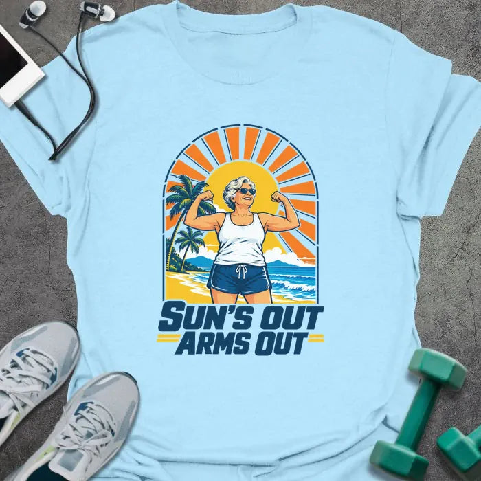 Light blue t-shirt printed with "SUN'S OUT ARMS OUT" in navy blue, with a retro beach sunset and an older woman flexing her arms