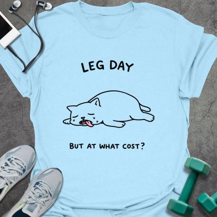 Light blue t-shirt printed with "Leg Day but at What Cost?" in black, with an illustration of a cat laying down