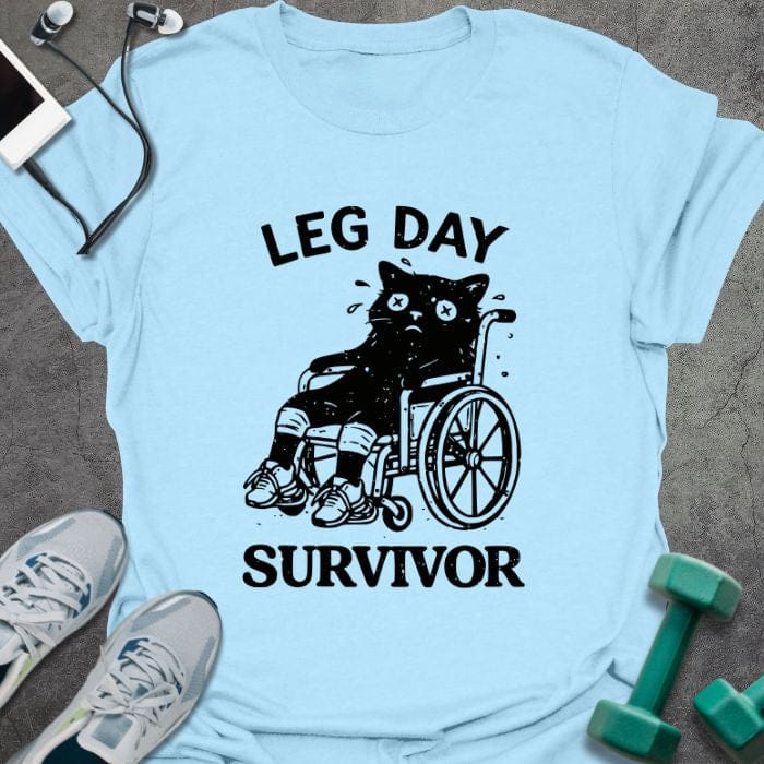 Light blue t-shirt printed with "Leg Day Survivor", with a black cat with X eyes sitting in a wheelchair with bandaged legs