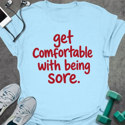 Light blue t-shirt printed with "get comfortable with being sore." in red