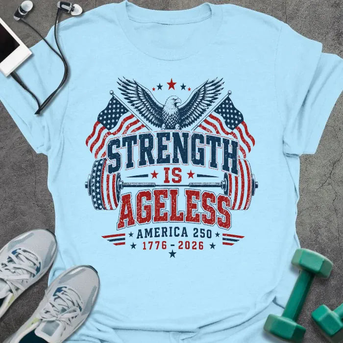 Light blue t-shirt printed with "Strength is Ageless America 250 1776 - 2026" in red and blue, with an eagle, American flags, and dumbbell