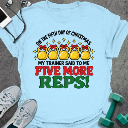 Light blue t-shirt printed with "ON THE FIFTH DAY OF CHRISTMAS MY TRAINER SAID TO ME, FIVE MORE REPS!" in black, red and green, with five gold kettlebells tied with red bows