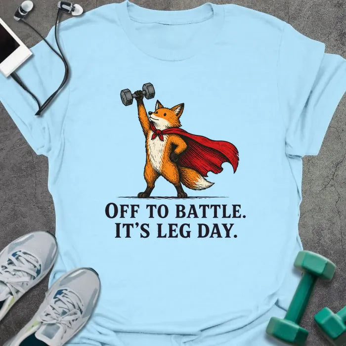 Light Blue t-shirt printed with "OFF TO BATTLE. IT'S LEG DAY." in black lettering, with a red fox wearing a red cape and holding a dumbbell