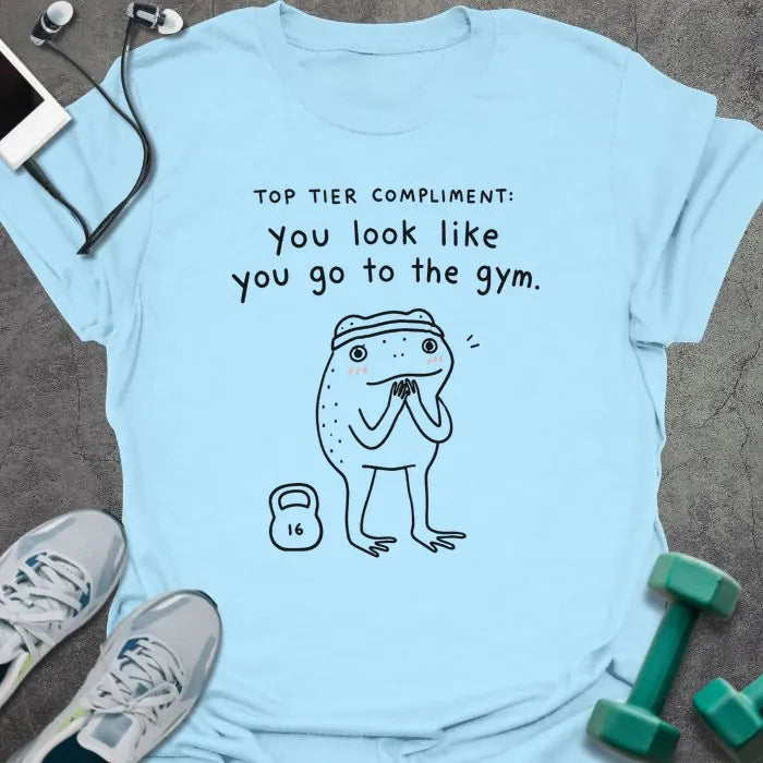 Light Blue t-shirt printed with "TOP TIER COMPLIMENT: you look like you go to the gym." in black, with frog graphic holding barbells