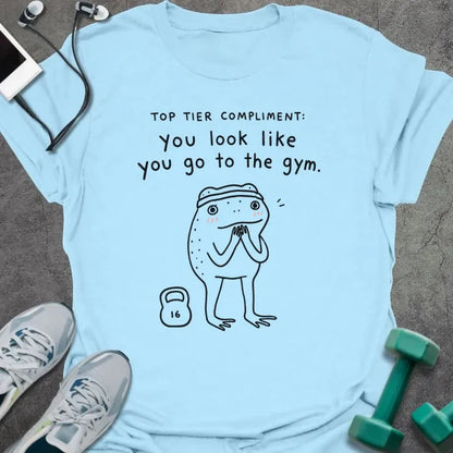 Light Blue t-shirt printed with "TOP TIER COMPLIMENT: you look like you go to the gym." in black, with frog graphic holding barbells