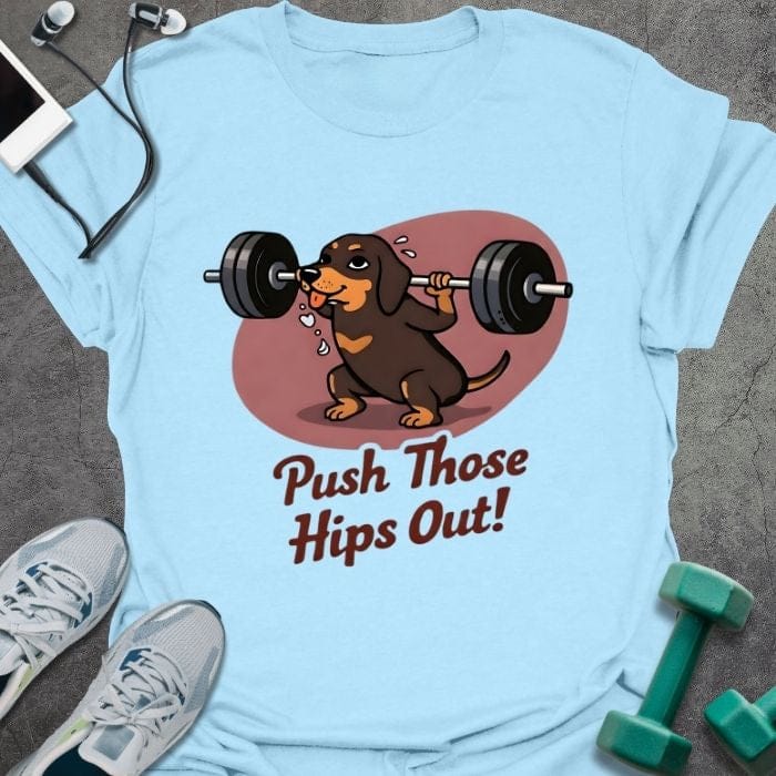 Light blue t-shirt printed with "Push Those Hips Out!" in tan, brown, with a dachshund lifting a barbell