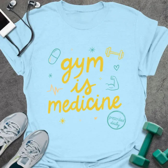 Light blue t-shirt printed with "gym is medicine" in yellow, cyan, and orange, with dumbbell, heartbeat, and smiley graphics