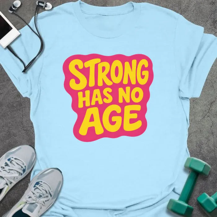 Light blue t-shirt printed with "STRONG HAS NO AGE" in yellow and pink, with badge graphic