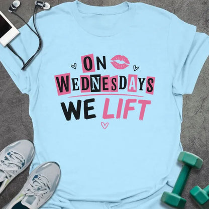 Light blue t-shirt printed with "On Wednesdays We Lift" in pink and black, with an illustration of lips and hearts
