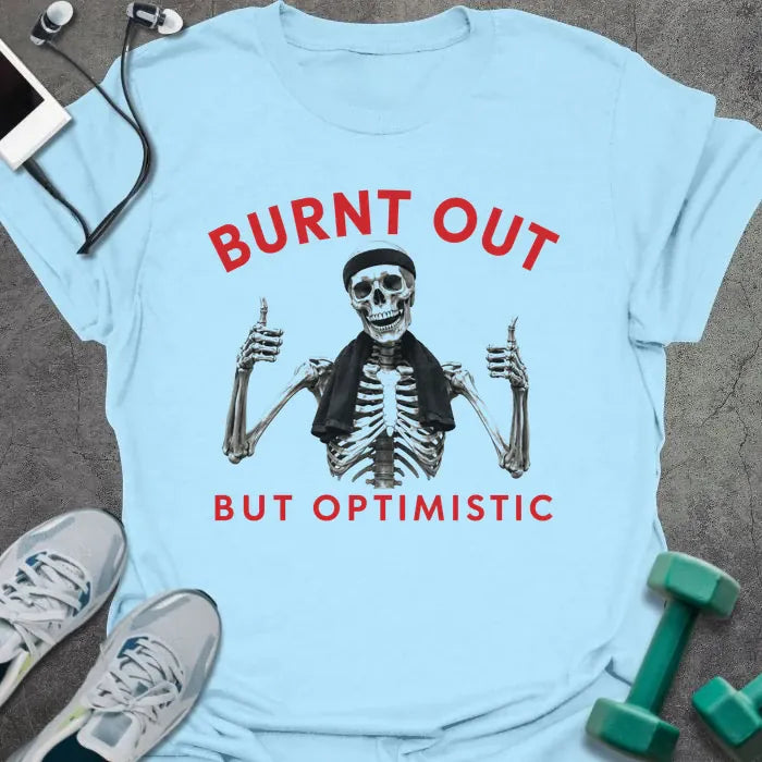Light Blue t-shirt printed with "BURNT OUT but OPTIMISTIC" in red and black, with skeleton with dumbbells