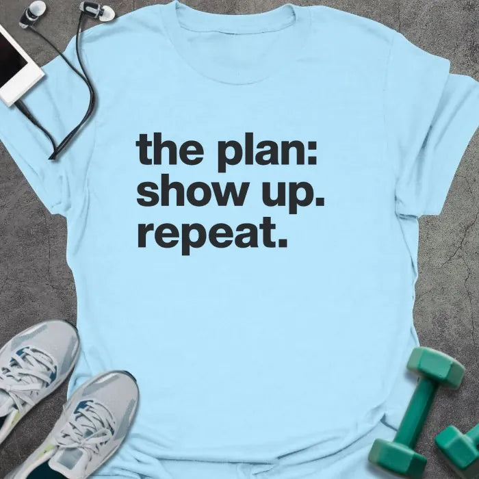 Light Blue t-shirt printed with "the plan: show up. repeat." in black lettering