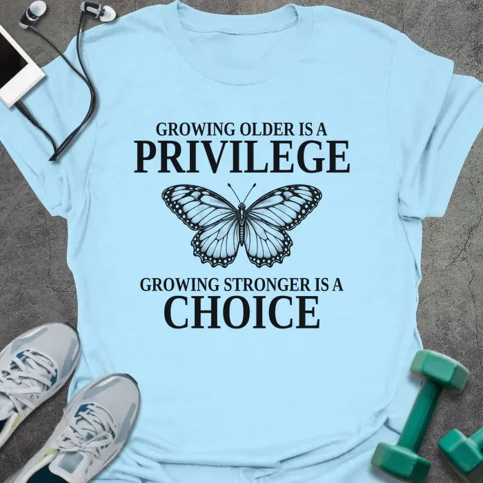 Light blue t-shirt printed with "GROWING OLDER IS A PRIVILEGE, GROWING STRONGER IS A CHOICE" in black, with a line-drawn butterfly