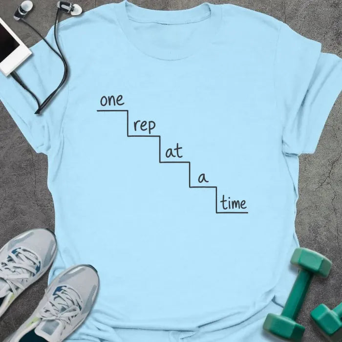 Light blue t-shirt printed with "one rep at a time" in black line art, with staircase graphic