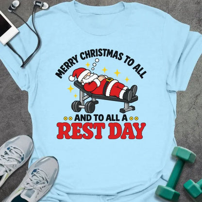 Light blue t-shirt printed with "MERRY CHRISTMAS TO ALL AND TO ALL A REST DAY" in black and red, with Santa asleep on a weight bench