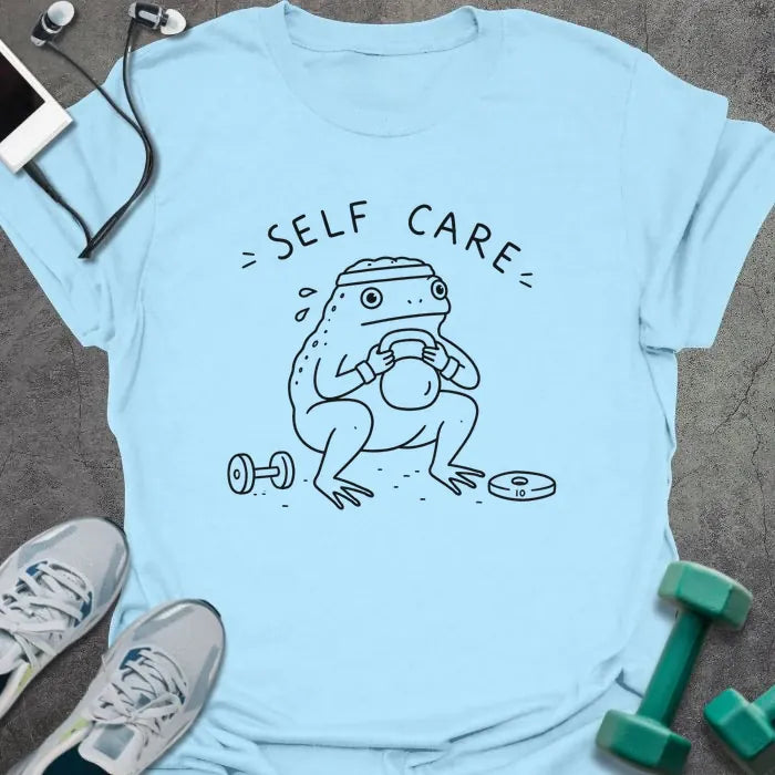 Light Blue t-shirt printed with "= SELF CARE =" in black, with figure exercising with kettlebell and dumbbells