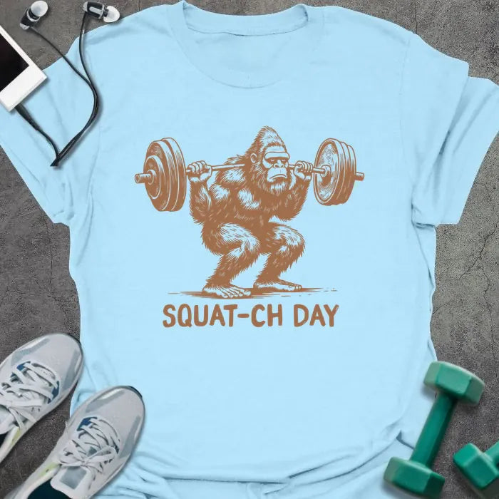Light blue t-shirt with an illustration of a sasquatch lifting barbell in rust