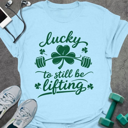 Light blue t-shirt printed with "lucky to still be lifting" in green, with clover, shamrock and barbell