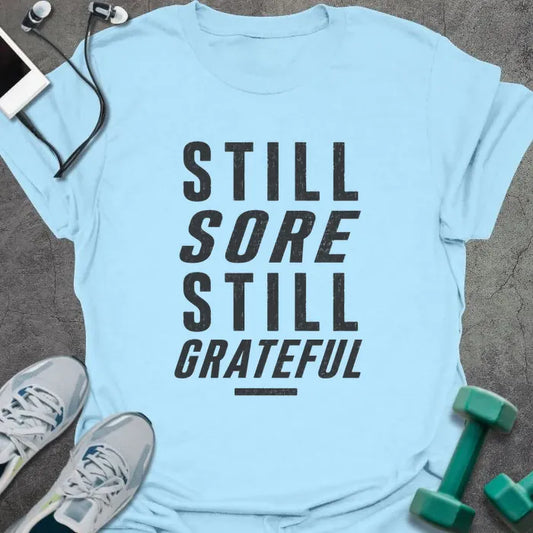 Light Blue t-shirt printed with "STILL SORE STILL GRATEFUL" in black bold caps with underline