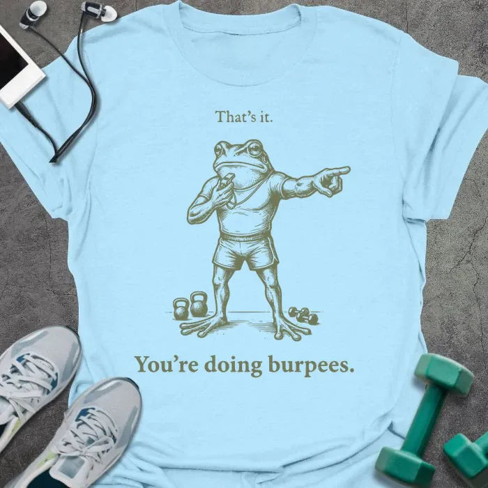 Light blue t-shirt printed with "That's it. You're doing burpees." in tan, with an illustration of a frog character in sportswear pointing