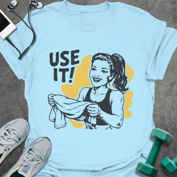 Light blue t-shirt printed with "Use it!" in black and yellow, with a retro-style woman illustration holding a towel