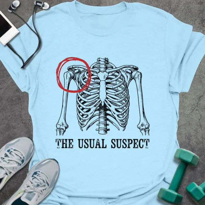 Light blue t-shirt printed with "The Usual Suspect" in white and red, with a skeleton anatomy illustration highlighting the heart in red