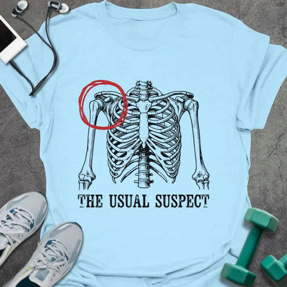 Light blue t-shirt printed with "The Usual Suspect" in white and red, with a skeleton anatomy illustration highlighting the heart in red