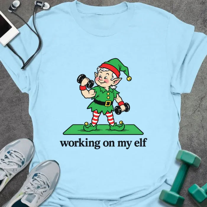 Light blue t-shirt printed with "working on my elf" in black, with a vintage elf lifting dumbbells on a green mat