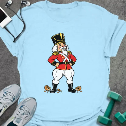 Light blue t-shirt printed with a vintage nutcracker soldier with strong legs, hands on hips, standing over cracked nutshells