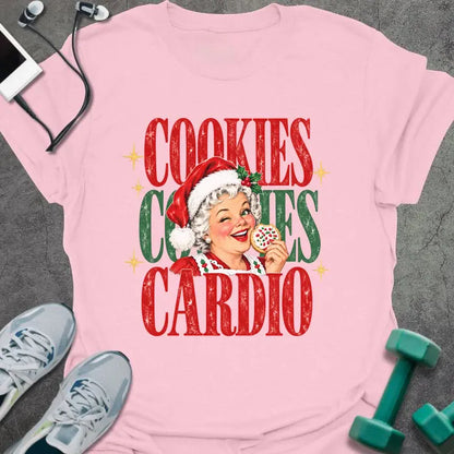 Light pink t-shirt printed with "COOKIES COOKIES CARDIO" in red and green, with a vintage Mrs. Claus in a Santa hat winking and holding a frosted cookie