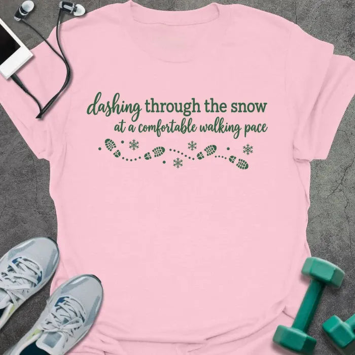 Light pink t-shirt printed with "dashing through the snow at a comfortable walking pace" in green, with a dotted trail of footprints and snowflakes