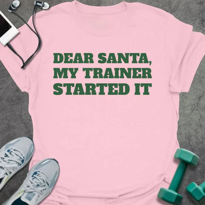 Light pink t-shirt printed with "DEAR SANTA, MY TRAINER STARTED IT" in green