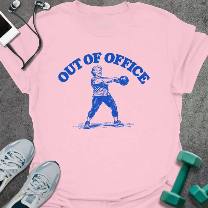 Light pink t-shirt printed with "OUT OF OFFICE" in blue, with a sketch of an older woman swinging a kettlebell