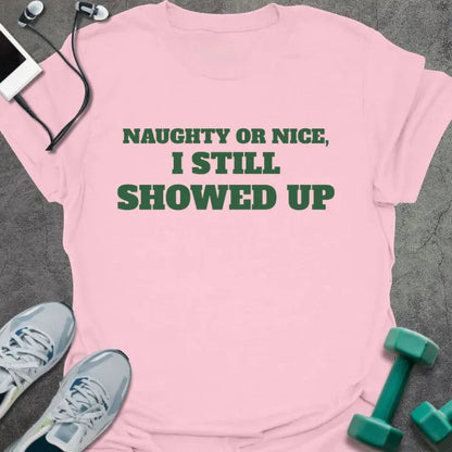 Light pink t-shirt printed with "NAUGHTY OR NICE, I STILL SHOWED UP" in green