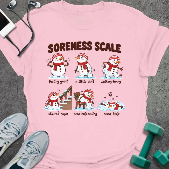 Light pink t-shirt printed with "SORENESS SCALE" in brown, with six snowmen in striped headbands and red scarves labeled feeling great, a little stiff, walking funny, stairs? nope, need help sitting, and send help