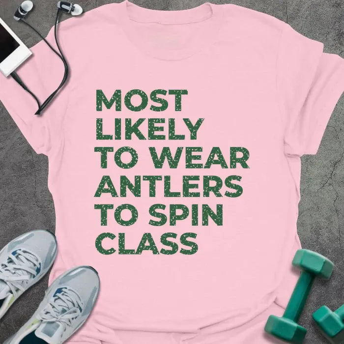 Light pink t-shirt printed with "MOST LIKELY TO WEAR ANTLERS TO SPIN CLASS" in green