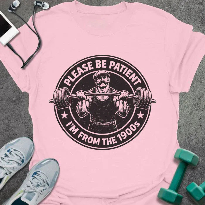 Light pink t-shirt printed with "Please Be Patient I'm From the 1900s" in black, with a barbells and a retro strongman illustration