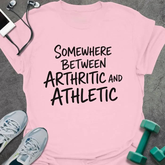 Light pink t-shirt printed with "SOMEWHERE BETWEEN ARTHRITIC AND ATHLETIC" in black