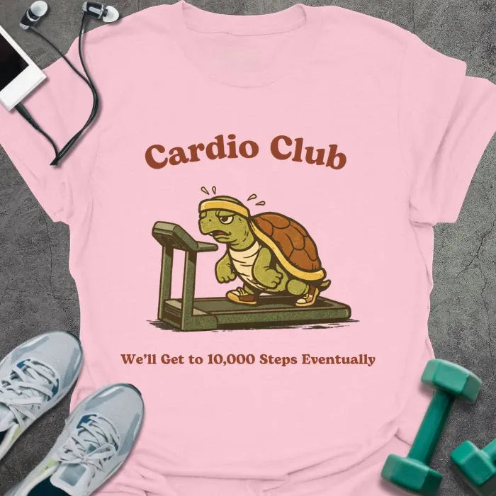 Light pink t-shirt printed with "Cardio Club We'll Get to 10,000 Steps Eventually" in brown and red, with turtle on treadmill graphic