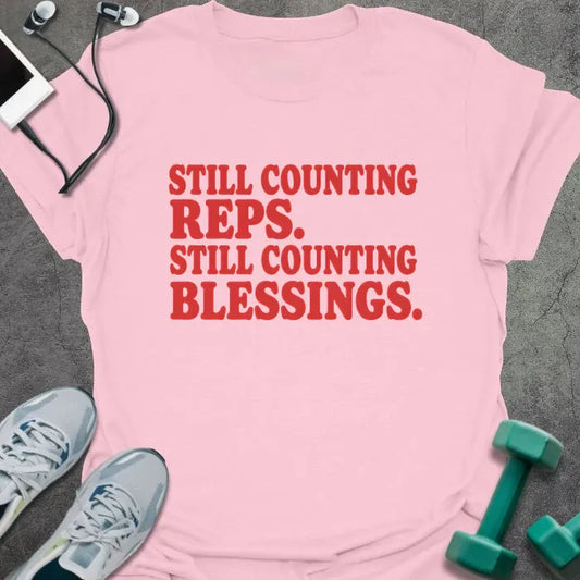 Light Pink t-shirt printed with "STILL COUNTING REPS. STILL COUNTING BLESSINGS." in red block lettering