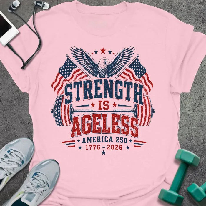 Light pink t-shirt printed with "Strength is Ageless America 250 1776 - 2026" in red and blue, with an eagle, American flags, and dumbbell