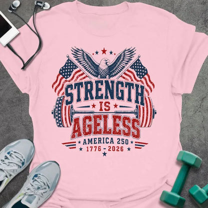 Light pink t-shirt printed with "Strength is Ageless America 250 1776 - 2026" in red and blue, with an eagle, American flags, and dumbbell