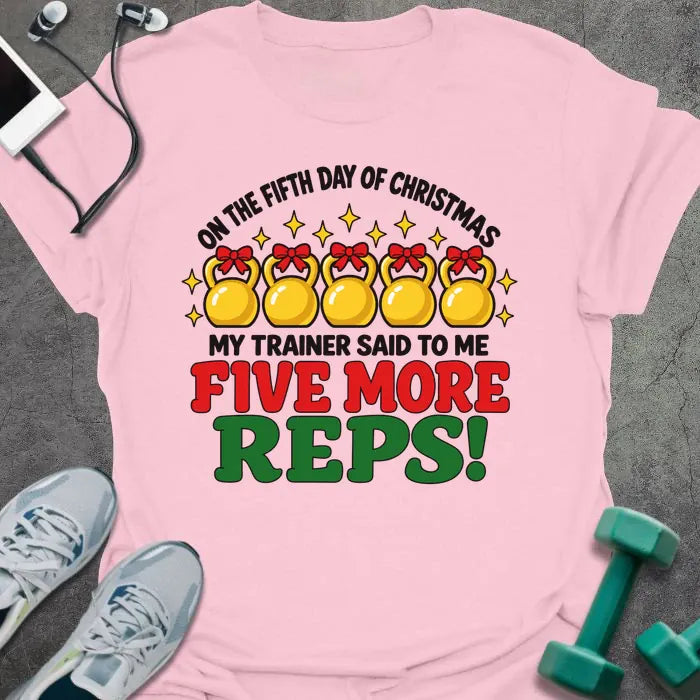 Light pink t-shirt printed with "ON THE FIFTH DAY OF CHRISTMAS MY TRAINER SAID TO ME, FIVE MORE REPS!" in black, red and green, with five gold kettlebells tied with red bows