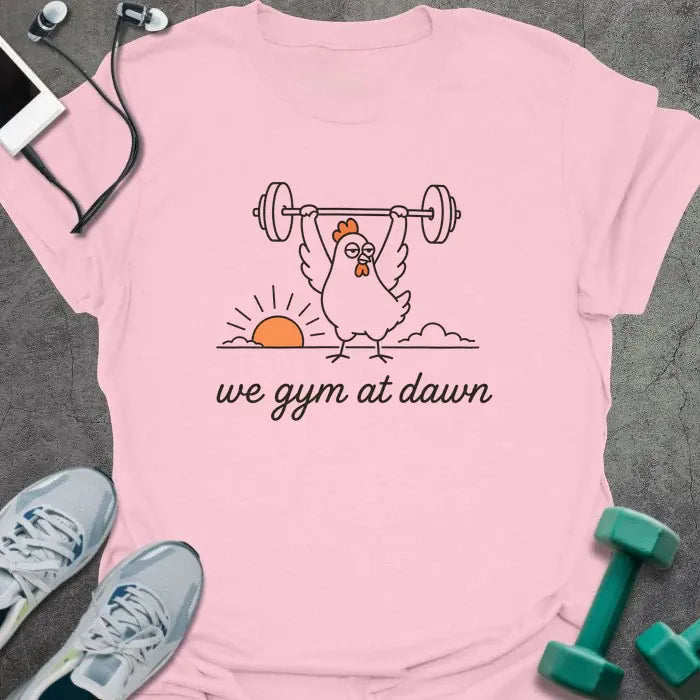 Light pink t-shirt printed with "we gym at dawn" in orange, with a bird lifting weights at sunrise