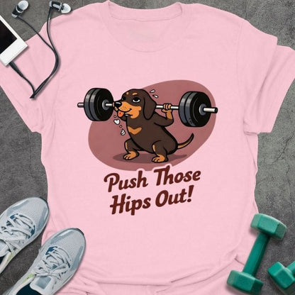Light pink t-shirt printed with "Push Those Hips Out!" in tan, brown, with a dachshund lifting a barbell