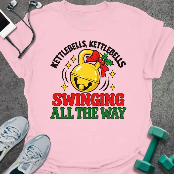 Light pink t-shirt printed with "KETTLEBELLS, KETTLEBELLS, SWINGING ALL THE WAY" in black, red and green, with a gold jingle bell kettlebell and holly