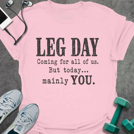 Light pink T-shirt printed with "LEG DAY Coming for all of us. But today... mainly YOU." in brown