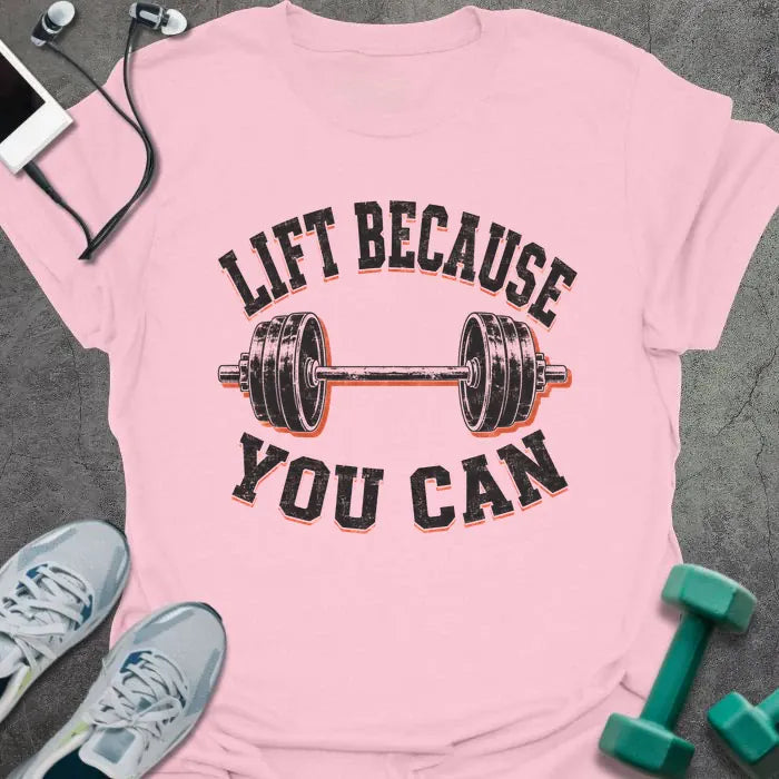 Light Pink t-shirt printed with "LIFT BECAUSE YOU CAN" in black and red text with a barbell graphic